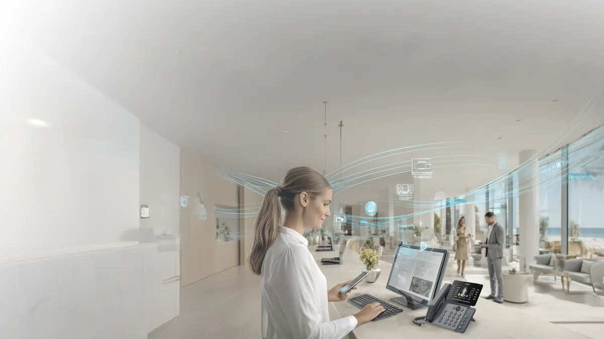 Recepcionista de hotel atendiendo con teléfono IP y tableta